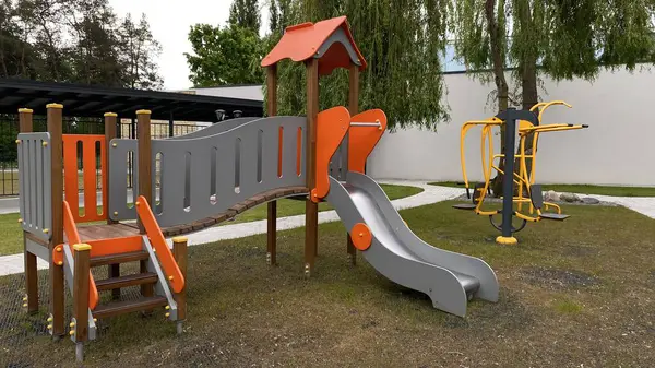 Renkli bir kaydırak, tırmanma merdiveni, küçük ahşap oyun evi ve köprü yapısı olan modern açık hava çocukları için oyun alanı. Kamu parkında ya da eğlence alanında geçen bu ekipman fiziksel aktiviteyi, hayal gücünü ve sosyal etkileşimi teşvik eder..