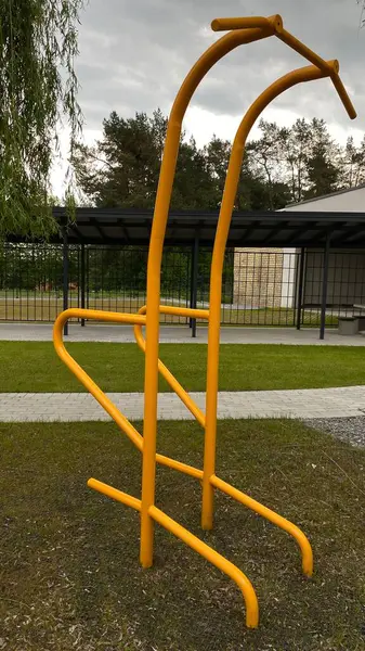 Modern bir konut avlusuna yerleştirilmiş sağlam metal paralel barlar, bir çocuk oyun parkının yakınında yer alıyor. Vücut ağırlık egzersizleri ve sokak fitness rutinleri için tasarlanan ekipman, fiziksel gelişimi destekliyor ve aktif bir kentsel yaşamı teşvik ediyor.