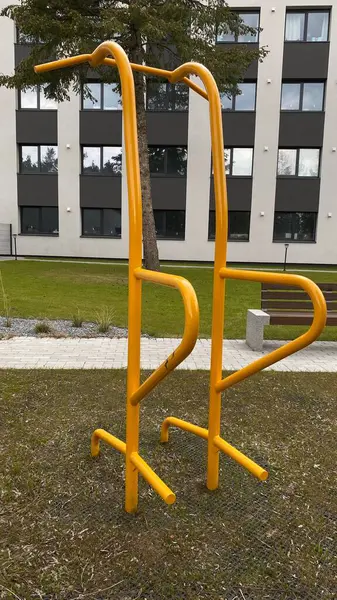 Modern bir konut avlusuna yerleştirilmiş sağlam metal paralel barlar, bir çocuk oyun parkının yakınında yer alıyor. Vücut ağırlık egzersizleri ve sokak fitness rutinleri için tasarlanan ekipman, fiziksel gelişimi destekliyor ve aktif bir kentsel yaşamı teşvik ediyor.