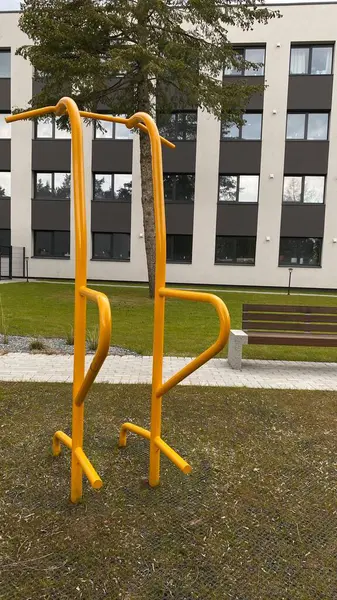 Modern bir konut avlusuna yerleştirilmiş sağlam metal paralel barlar, bir çocuk oyun parkının yakınında yer alıyor. Vücut ağırlık egzersizleri ve sokak fitness rutinleri için tasarlanan ekipman, fiziksel gelişimi destekliyor ve aktif bir kentsel yaşamı teşvik ediyor.