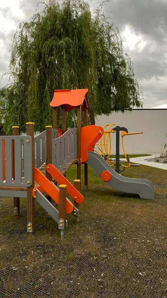 Renkli bir kaydırak, tırmanma merdiveni, küçük ahşap oyun evi ve köprü yapısı olan modern açık hava çocukları için oyun alanı. Kamu parkında ya da eğlence alanında geçen bu ekipman fiziksel aktiviteyi, hayal gücünü ve sosyal etkileşimi teşvik eder..