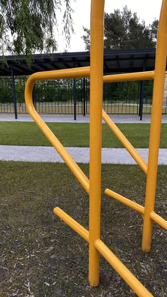 Modern bir konut avlusuna yerleştirilmiş sağlam metal paralel barlar, bir çocuk oyun parkının yakınında yer alıyor. Vücut ağırlık egzersizleri ve sokak fitness rutinleri için tasarlanan ekipman, fiziksel gelişimi destekliyor ve aktif bir kentsel yaşamı teşvik ediyor.