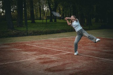 Genç bir kız açık hava kil kortunda tenis topuna raketle vuruyor. Saray yeşil bir orman ve tel örgü ile çevrili. Sıradan bir kot pantolon ve beyaz bir tişört giyip bahar etkinliğinin tadını çıkarıyor.. 