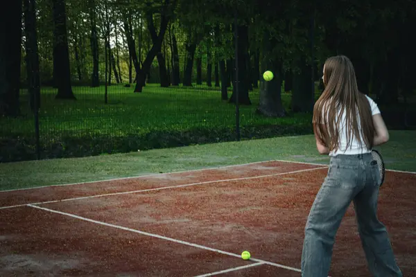 Genç bir kız açık hava kil kortunda tenis topuna raketle vuruyor. Saray yeşil bir orman ve tel örgü ile çevrili. Sıradan bir kot pantolon ve beyaz bir tişört giyip bahar etkinliğinin tadını çıkarıyor.. 