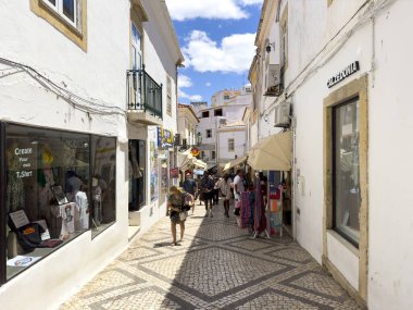 Albufeira, Portekiz, 26 Haziran 2024 - yerel dükkanlar arasında turistlerin dolaştığı şehir merkezi dar cadde.