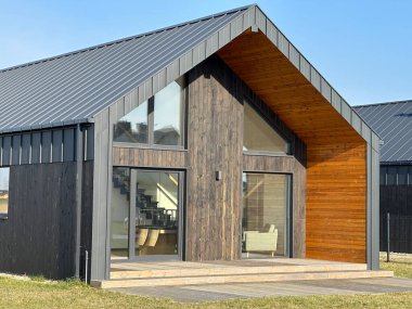 Görüntü, kırsal bir alanda yer alan parlak cam cepheli şık ve modern bir evi tasvir ediyor. Özenle tasarlanmış ortamlar cazibesini arttırır.