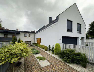 Modern bir ev cephesi, ilginç asfalt yolu olan büyük bir aile evi. Bitkiler ve çalılarla ön bahçe düzenlemeleri.