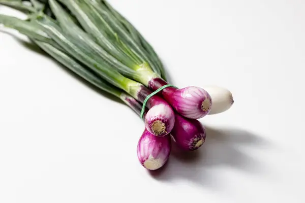 stock image Close-up view of a bunch of fresh red onions with purple and white bulbs, tied together and set against a clean white background. Ideal for culinary, gardening, and healthy eating concepts