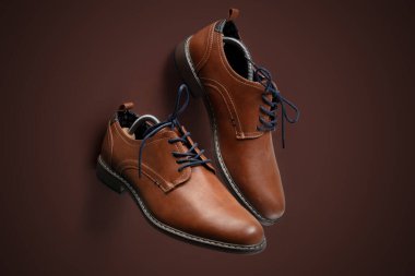 Siyah tabanlı ve koyu bağcıklı şık kahverengi deri ayakkabılar. Kahverengi arka planda sunuluyor. Klasik ayakkabı, resmi etkinlikler, ofis kıyafetleri veya moda içeriği için idealdir. Yüksek kaliteli stüdyo ışıklandırması dokuyu vurguluyor