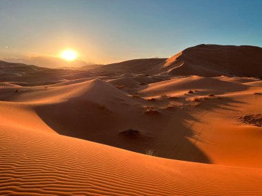 Sahra Çölü 'ndeki kum tepeleri, Merzouga Çölü, kum tepelerinde küçük dalgalar oluşturan kum taneleri, panoramik manzara. Güneş batıyor. Fas 'ta. Objektif objektife güneşin yansımaları