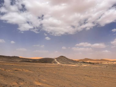 Merzouga, Erg Chebbi dunes, Morocco, Africa: panoramic road in the Sahara desert in the Black Mountain area, with view of the black stones, fossils and sand dunes, 4x4 trip, blue sky and white clouds