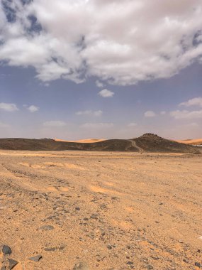 Merzouga, Erg Chebbi dunes, Morocco, Africa: panoramic road in the Sahara desert in the Black Mountain area, with view of the black stones, fossils and sand dunes, 4x4 trip, blue sky and white clouds