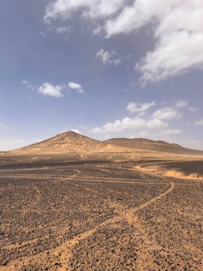 Merzouga, Erg Chebbi dunes, Morocco, Africa: panoramic road in the Sahara desert in the Black Mountain area, with view of the black stones, fossils and sand dunes, 4x4 trip, blue sky and white clouds