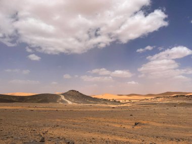 Merzouga, Erg Chebbi dunes, Morocco, Africa: panoramic road in the Sahara desert in the Black Mountain area, with view of the black stones, fossils and sand dunes, 4x4 trip, blue sky and white clouds