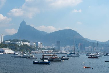 Rio de Janeiro, Brezilya, 06-07-2023: Urca bölgesi, Guanabara Körfezi manzarası ve sisli şehir silueti olan balıkçı tekneleri limanı ve arka planda Corcovado Dağı 'ndaki Kurtarıcı İsa 