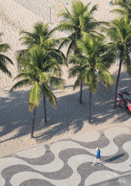 Rio de Janeiro, Brezilya, 06-07-2023: Copacabana sahilinin ikonik grafik kaldırımında yürüyen bir kadın, Avenida Atlantica (Atlantik Bulvarı) boyunca, kum ve palmiye ağaçları ile 