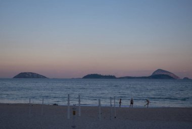 Rio de Janeiro, Brezilya, 07-06-2023: Dünyanın en ünlü plajlarından biri olan Ipanema plajında insanlar Avenida Atlantica ve palmiye ağaçları boyunca ikonik grafik kaldırımları ile gün batımında oynuyorlar.