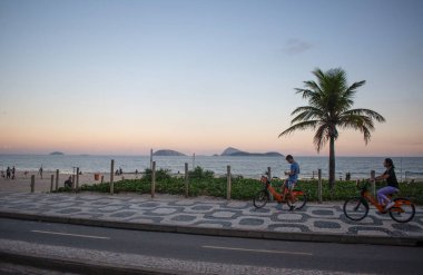 Rio de Janeiro, Brezilya, 06-07-2023: dünyanın en ünlü plajlarından biri olan Ipanema plajında bisiklet sürmek, Avenida Atlantica (Atlantik Bulvarı) boyunca ikonik grafik kaldırımı ve palmiye ağaçları ile