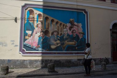 Rio de Janeiro, Brezilya, 06-07-2023: Lapa sokaklarındaki kadın arka planda Arcos da Lapa olarak bilinen Carioca Aqueduct ile Brezilya müziğine adanmış bir duvar resmi arıyor.
