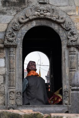 Katmandu, Nepal, 10-03-2023: Bir ailenin kutsal Bagmati nehri boyunca ölüler için hediye hazırlamasını bekleyen bir Brahman, Pashupatinath Tapınağı 'nda yakma töreni, Shiva' ya adanmış bir Hindu tapınağı.