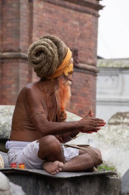 Kathmandu, Nepal, 10-03-2023: bacak bacak bacak bacak üstüne atarak bir aile bekliyor Bagmati nehri boyunca ölüler için hediyeler hazırlayın, Pashupatinath Tapınağı 'nda yakma töreni, Shiva' ya adanmış Hindu tapınağı