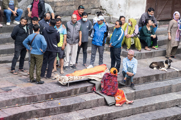 Kathmandu, Nepal, 10-03-2023: family with washed and bandaged body of the dead on a stretcher along sacred Bagmati river, cremation ceremony at Pashupatinath Temple, Hindu temple dedicated to Shiva