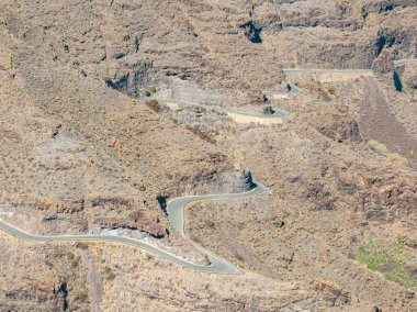 Gran Canaria 'nın batı kıyısındaki virajlı yolların hava manzarası, en az kentleşmiş sahil. Mogan Eyaleti. Az bitki örtüsü olan çöl arazisi, seyrek yerleşim olan vadilerle değişen dağlar..