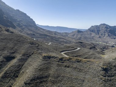 Gran Canaria 'nın batı kıyısındaki virajlı yolların hava manzarası, en az kentleşmiş sahil. Mogan Eyaleti. Az bitki örtüsü olan çöl arazisi, seyrek yerleşim olan vadilerle değişen dağlar..