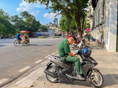 Hanoi, Vietnam, 10-11-2024: daily life in the streets, a soldier seated on a motorbike while traffic jam on the day of the 70th anniversary of the liberation of the capital from the French (1954-2024) clipart