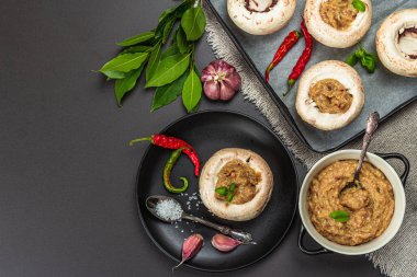 Çiğ mantar kapları pişirmeye hazır. Taze şampiyonlar, baharatlar, sebzeler. Yemek pişirme süreci, modaya uygun sert ışık, karanlık gölge. Siyah taş arkaplan, üst görünüm