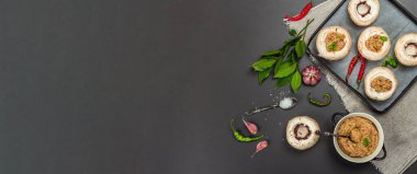 Çiğ mantar kapları pişirmeye hazır. Taze şampiyonlar, baharatlar, sebzeler. Yemek pişirme süreci, modaya uygun sert ışık, karanlık gölge. Siyah taş arkaplan, pankart biçimi