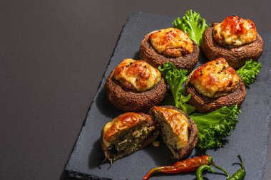 Pişmiş mantar kapları yenmeye hazır. Şampiyonlar, baharatlar, sebzeler, peynir. Hizmet edilen bölüm, modaya uygun sert ışık, karanlık gölge. Siyah taş arkaplan, boşluğu kopyala