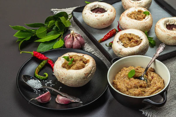 Raw stuffed mushroom caps ready for baking. Fresh champignons, spices, vegetables. Cooking process, trendy hard light, dark shadow. Black stone concrete background, close up