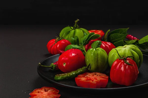 stock image Green and red ribbed tomatoes, American or Florentine variety. Ripe vegetables, chili, fresh bay leaves. Trendy hard light, dark shadow, stone concrete background, flat lay, copy space