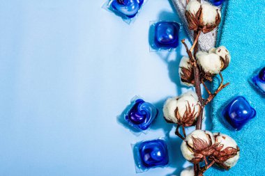 Makine yıkama konsepti. Deterjanlı kapsüller, yumuşak havlular ve pamuk çiçekleri. Çamaşır kapsülleri, sıvı renkli jel. Çevre dostu giysiler yıkama, düz yatak. Mavi arkaplan, üst görünüm