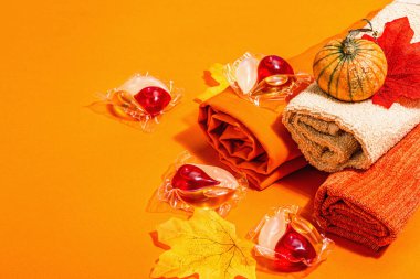 Makine yıkama konsepti. Deterjanlı kapsüller, yumuşak havlular ve sonbahar dekoru. Çamaşır kapsülleri, geleneksel sonbahar tarzı. Eko dostu çamaşır yıkama. Turuncu arkaplan, kopyalama alanı