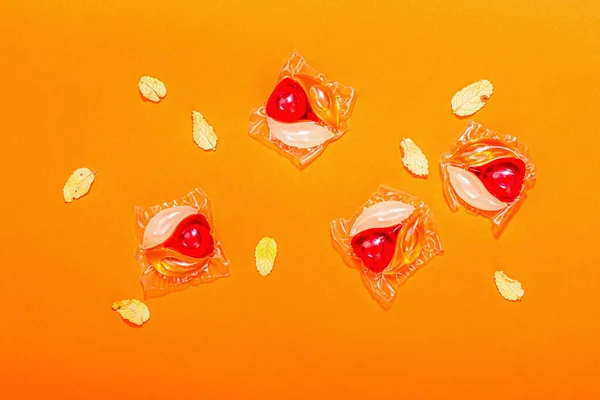 stock image Machine washing concept. Capsules with detergent and autumn decor. Laundry pods, traditional fall style. Eco friendly clothes washing. Orange background, top view