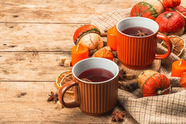 Spicy hot tea. Autumn good mood, traditional fall beverage in cups. Pumpkin, scarf, candles, star anise, cinnamon. Wooden boards background, copy space
