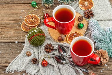 Winter cozy composition with hot tea and traditional Christmas decoration. New Year balls, fir trees, oranges and pine cones. Rustic style, old wooden background, copy space clipart