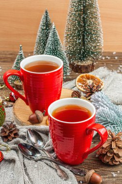 Sıcak çay ve geleneksel Noel süsüsüyle kış kompozisyonu. Yeni yıl baloları, köknar ağaçları, portakallar ve kozalaklar. Kırsal tarz, eski ahşap arka plan, yakın plan.