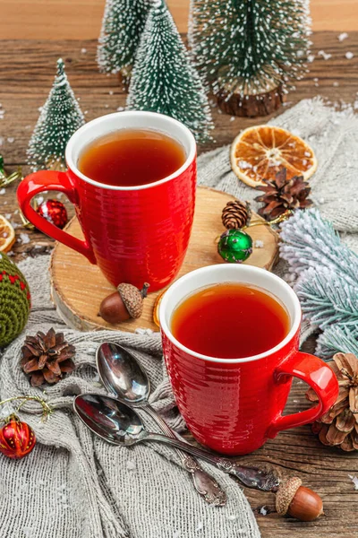 stock image Winter cozy composition with hot tea and traditional Christmas decoration. New Year balls, fir trees, oranges and pine cones. Rustic style, old wooden background, close up