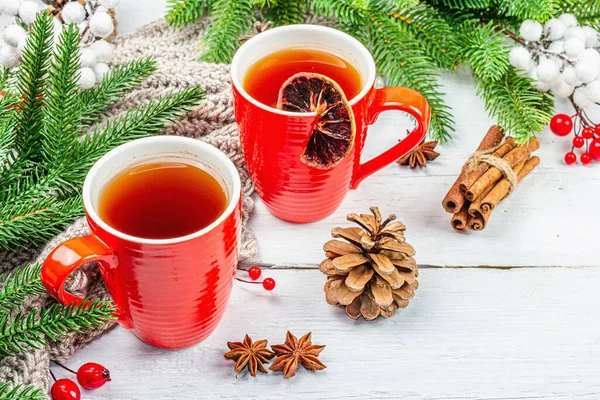 stock image Hot winter or Christmas tea in ceramic red cups. Fir tree branches, lemon slice, spices and berries. Traditional New Year decor, white wooden background, copy space
