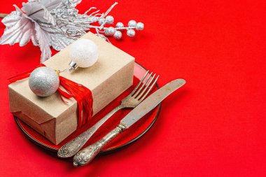 Noel sofrasında kırmızı ve gümüş renkli bir hediye kutusu var. Yeni yıl arkaplanı, seramik tabak ve geleneksel dekor. Düz konum, el yapımı tasarım, kopyalama alanı