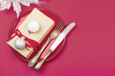 Noel sofrasında, modaya uygun Viva Magenta renginde bir hediye kutusu var. Yeni yıl arkaplanı, seramik tabak ve geleneksel dekor. Düz konum, el yapımı tasarım, üst görünüm