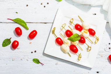 Geleneksel sağlıklı İtalyan aperatifi. Mozzarella, taze yapraklar ve şiş domatesler. Modern sert ışık, karanlık gölge, beyaz ahşap zemin, üst görünüm