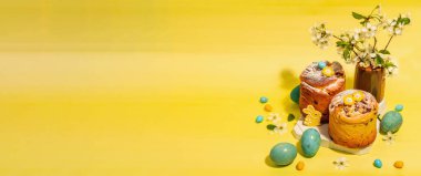 Paskalya keki Cruffin veya tatlı ekmek kulich. Geleneksel şenlikli pişirme ve vazoda çiçek açan kiraz dalları. Modaya uygun sert ışık, koyu gölge, parlak sarı arkaplan, afiş biçimi