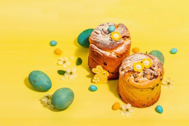 Easter cake Cruffin or sweet bread kulich and traditional painted eggs. Festive baking and cherry flowers. Trendy hard light, dark shadow, bright yellow background, copy space clipart