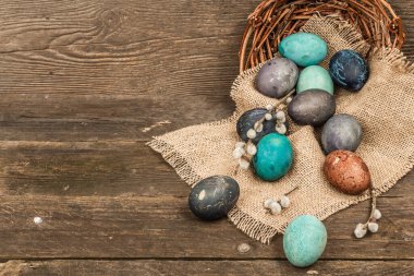 Hasır sepette paskalya yumurtaları ve eski ahşap arka planda kiraz çiçekleri. Kutlama kartı, geleneksel bahar sembolü. Modern sert ışık, karanlık gölge, düz yatış, kopyalama alanı