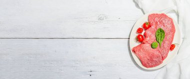 Raw veal steak with spices and cherry tomatoes. A trendy hard light, dark shadow, white wooden background, flat lay, banner format