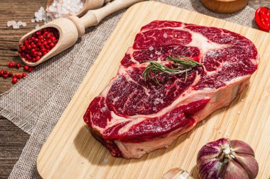 Raw Ribeye steak with spices and herbs. Dry aged meat, traditional food for grill. A trendy hard light, dark shadow, old wooden background, flat lay, close up